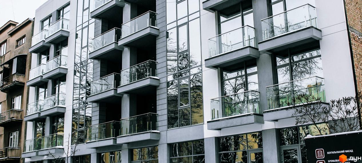 Фасад житлового комплексу Shevchenko з балконами та скляними елементами. Зовнішній вигляд новобудови з великими вікнами, що відображають дерева.