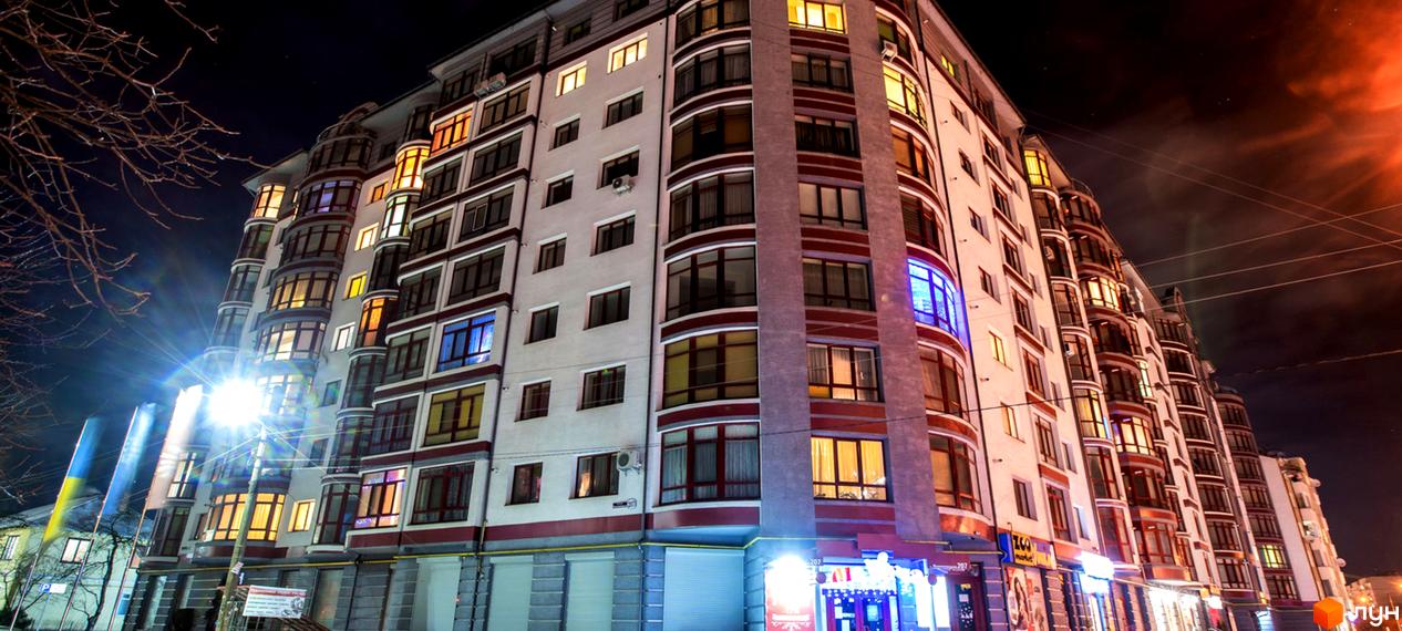 Зображення фасаду багатоповерхового будинку на вул. Вовчинецькій. Житловий комплекс з великими вікнами та червоними акцентами вночі.