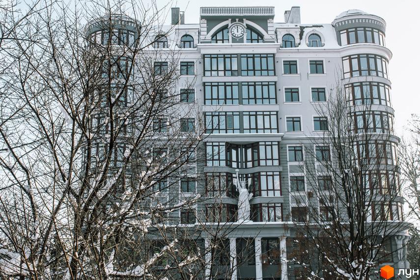 Фасад житлового комплексу Статус з великою кількістю вікон та архітектурними елементами. На передньому плані видно голі дерева, вкриті снігом.