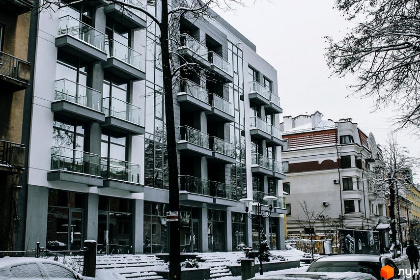 Зовнішній вигляд новобудови ЖК Shevchenko взимку, з засніженими сходами та деревами. Сучасна архітектура з великими вікнами та скляними балконами.