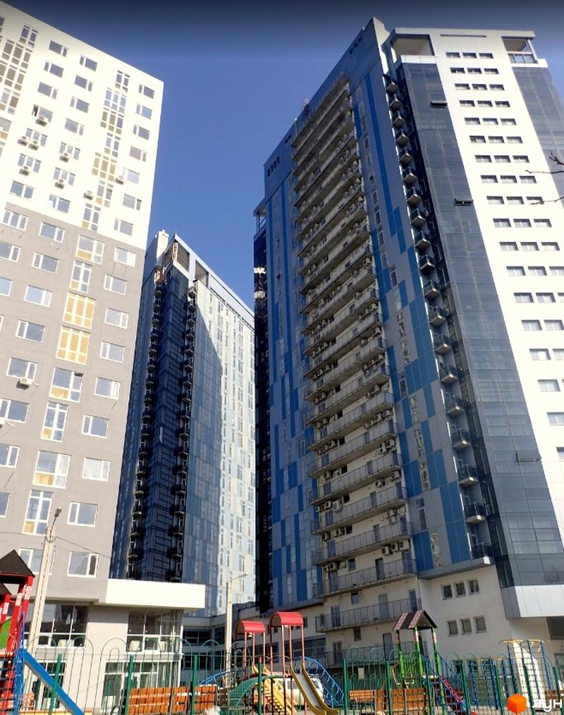 Високі житлові будинки Житлового комплексу Ультра з балконами та скляними фасадами. На передньому плані дитячий майданчик з гірками та гойдалками.