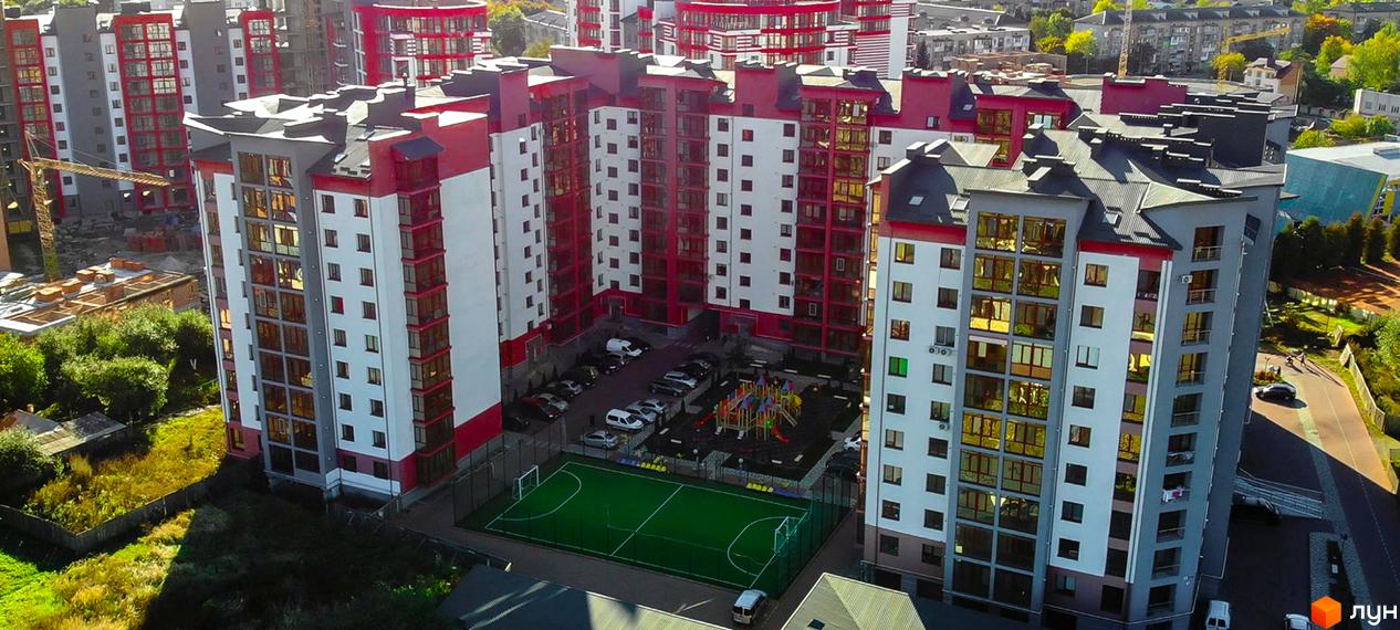 Зображення Житлового комплексу Європейський city: багатоповерхові будинки з червоно-білим фасадом, дитячий майданчик та футбольне поле на території.