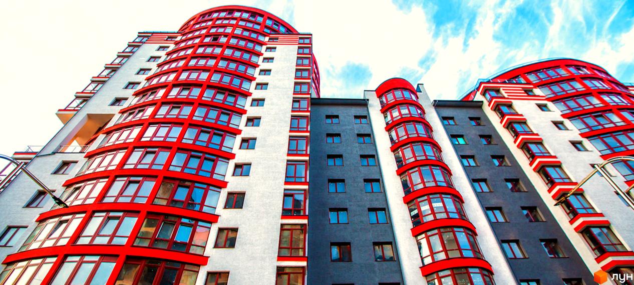 Зображення фасаду житлового комплексу Європейський city. Багатоповерховий будинок з червоними віконними рамами на фоні блакитного неба.