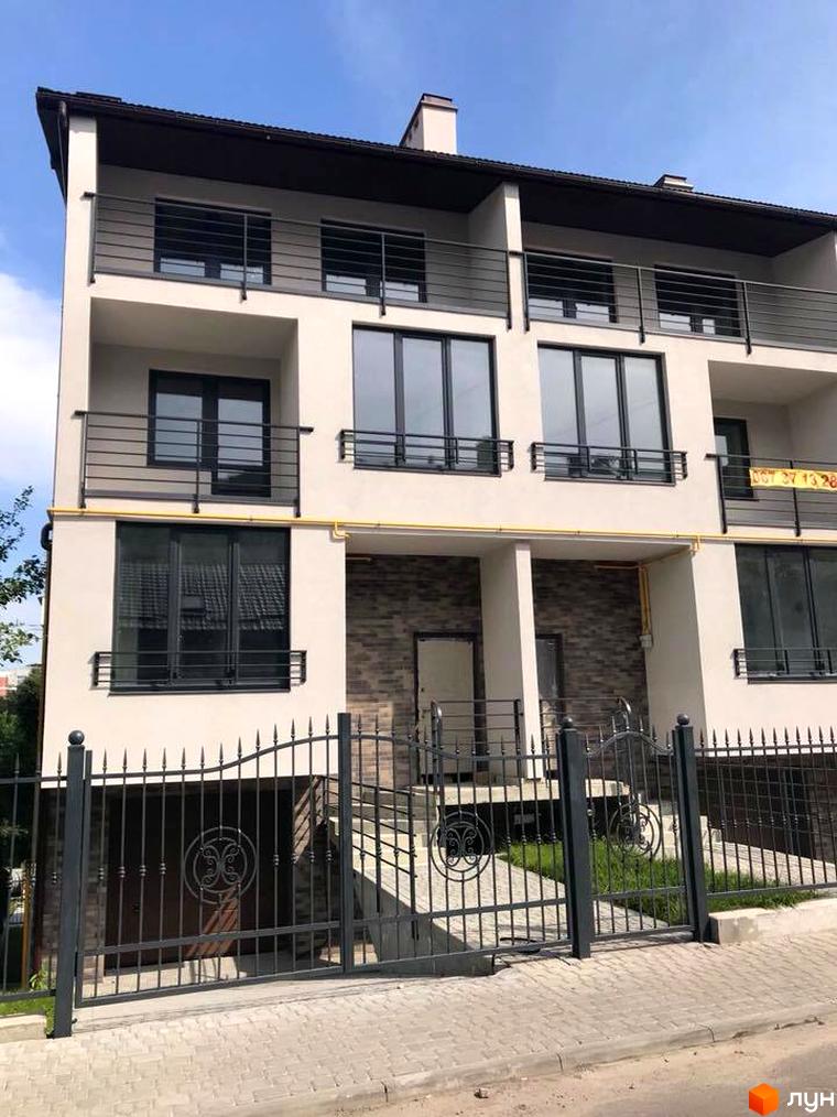 Таунхауси „На Куликівській“ з бежевим фасадом, темними вікнами та балконами з металевими поручнями. Перед будинком розташований металевий паркан та вимощена територія.