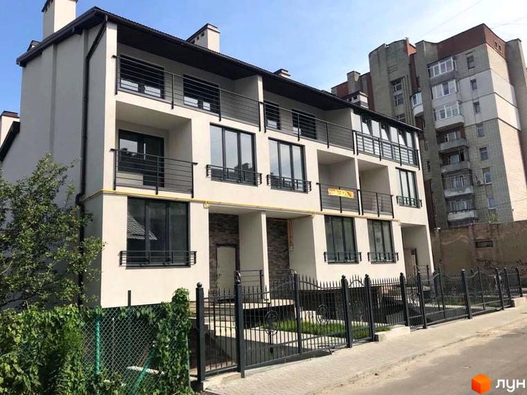 Таунхауси „На Куликівській“: триповерховий будинок зі світлим фасадом, чорними перилами балконів та великими вікнами. Перед будинком є металева огорожа та зелень.