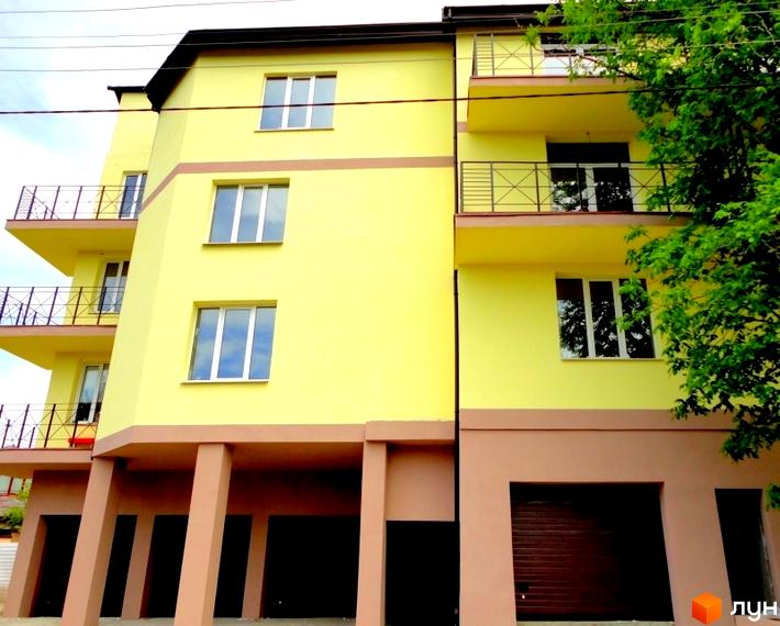 Житловий комплекс Тихорецький з жовтою фасадною стіною та балконами. Прибудинкова територія озеленена деревами.