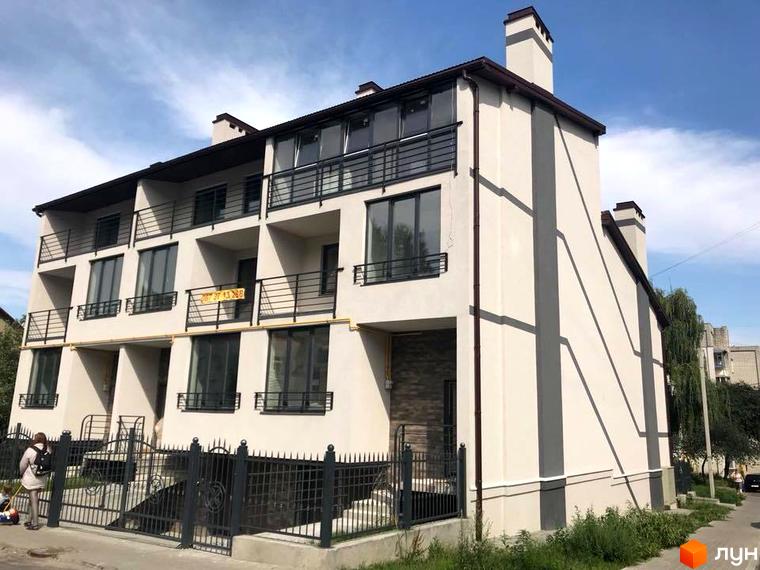 Таунхауси „На Куликівській“: багатоквартирний будинок світлого кольору з темними смугами, балконами та великими вікнами. Перед будинком металевий паркан.