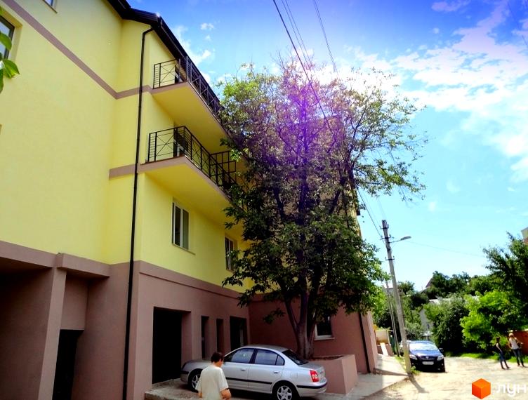 Житловий комплекс Тихорецький з жовтою фасадною стіною та балконами. Прибудинкова територія з зеленими насадженнями та автомобілями.