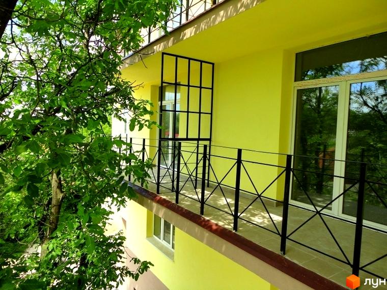 Житловий комплекс Тихорецький. Зовнішній вигляд будинку з жовтим фасадом, балконом та вікнами. Навколо зелені дерева.