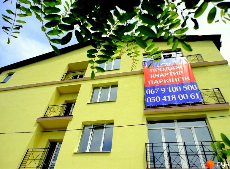 Житловий комплекс ЖК Тихорецький. Зовнішній вигляд жовтої багатоповерхівки з балконами та вікнами. На фасаді висить банер про продаж квартир та паркінгу.