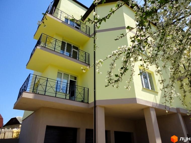 Житловий комплекс Тихорецький. Зовнішній вигляд світло-жовтого будинку з балконами та квітучими деревами на тлі блакитного неба.