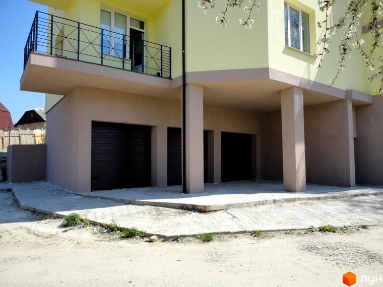 Зовнішній вигляд будинку ЖК Тихорецький з гаражними воротами та балконом. Прибудинкова територія з бетонною доріжкою та зеленню.