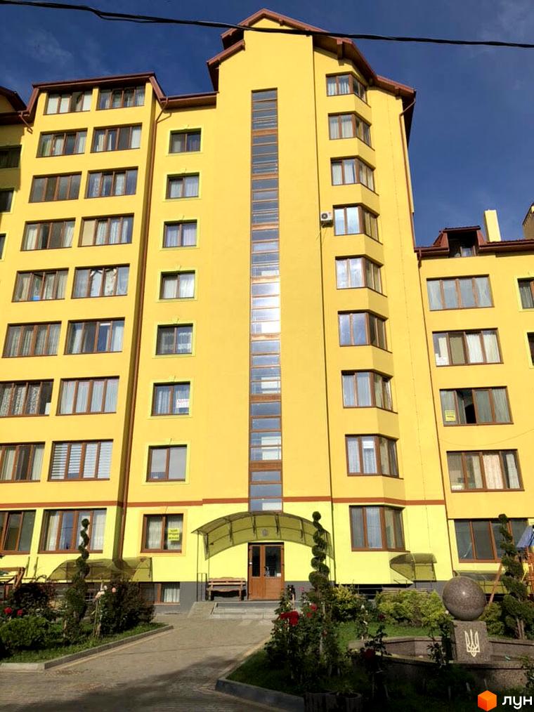 Житловий комплекс на вул. Помірецька, 9, з яскраво-жовтим фасадом та коричневими вікнами. Прибудинкова територія має зелені насадження та пам'ятний знак.