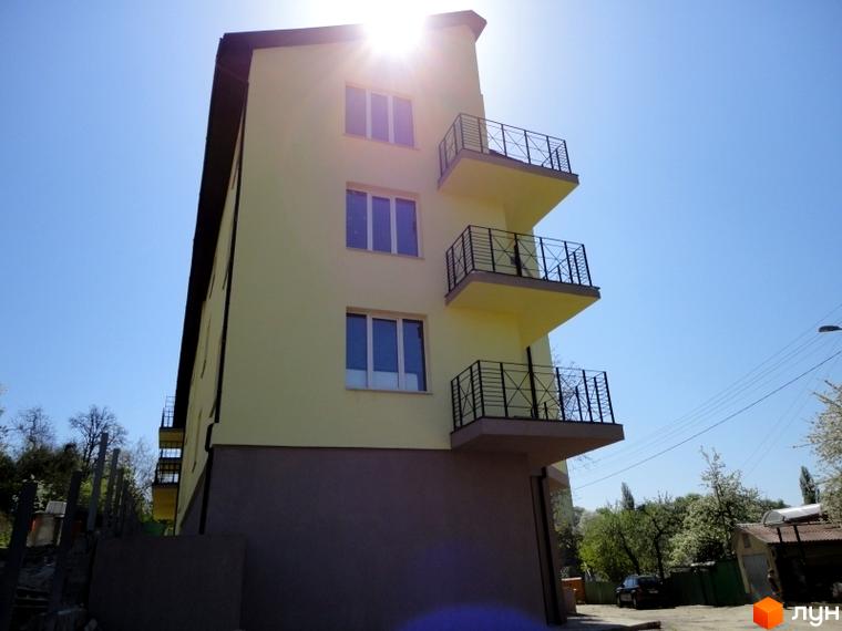 Будинок з жовтим фасадом та балконами. На прибудинковій території видно дерева та автомобіль.