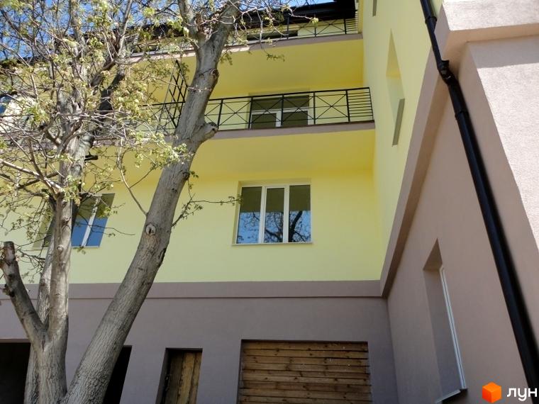 Житловий комплекс Тихорецький. Фасад будинку з жовтими стінами, балконами з чорними перилами та вікнами. Поруч ростуть дерева.