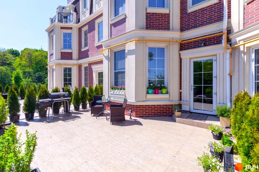 Таунхауси Royal Hill з червоної цегли та світлими фасадами. На прибудинковій території розташовані зелені туї, мангал та зона відпочинку з плетеними меблями.