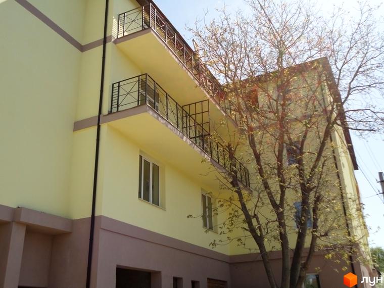 Фасад новобудови ЖК Тихорецький з балконами та вікнами. На передньому плані дерево з молодим листям.