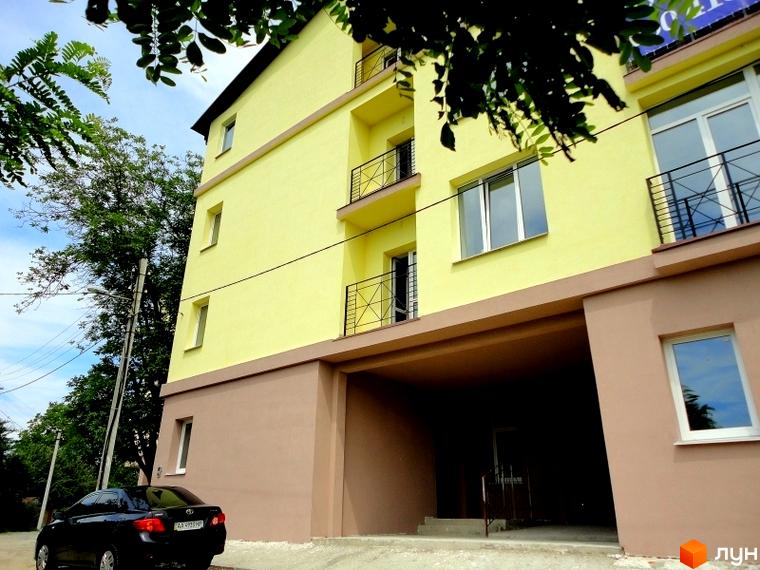 Житловий комплекс ЖК Тихорецький - новий жовтий будинок з коричневим цоколем та балконами. Поруч зелені дерева та чорний автомобіль.