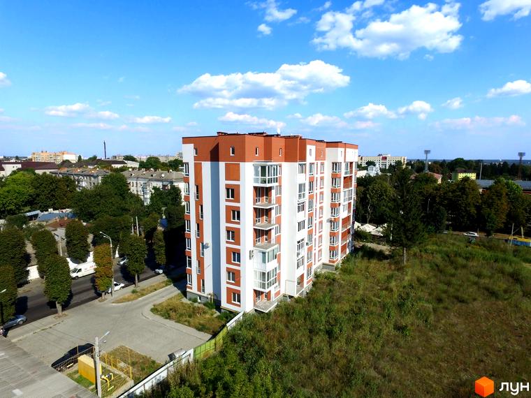 Висотна новобудова ЖК Сіті Парк з білими фасадами та коричневим дахом. Навколо будинку зелені насадження та прибудинкова територія.