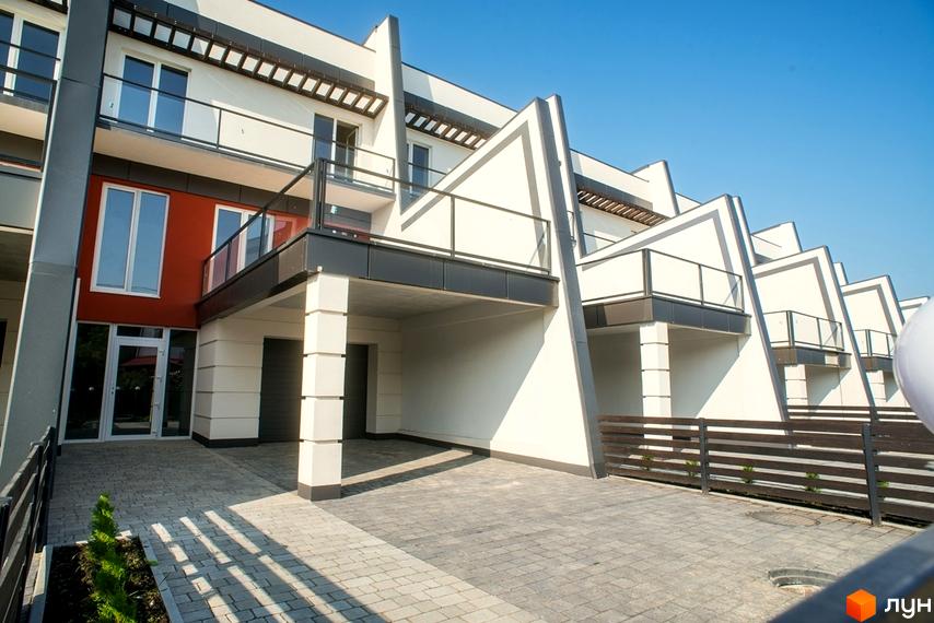 Ряд таунхаусів Капітель з білими фасадами, темними елементами та балконами. Видно вимощену бруківкою прибудинкову територію.