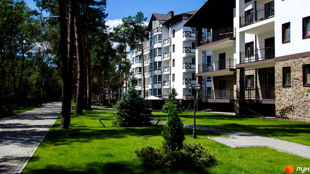 Житловий комплекс DESNA residence з білими фасадами, кам'яним оздобленням та балконами. Прибудинкова територія з доглянутим газоном, зеленими ялинками та доріжками.