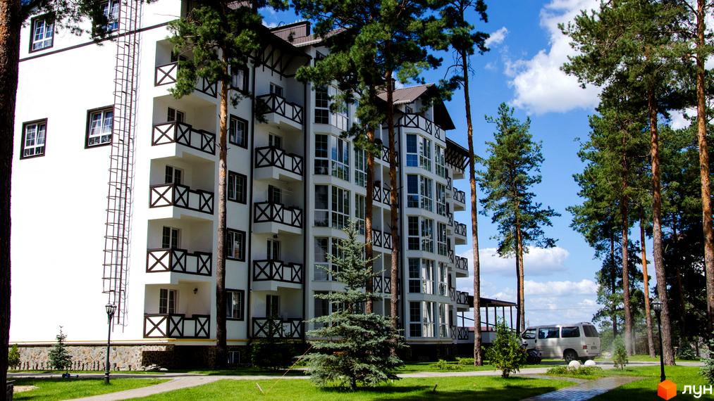 Житловий комплекс DESNA residence з білим фасадом, темними балконними огорожами та великими вікнами. Навколо комплексу зелена прибудинкова територія з деревами та доріжками.