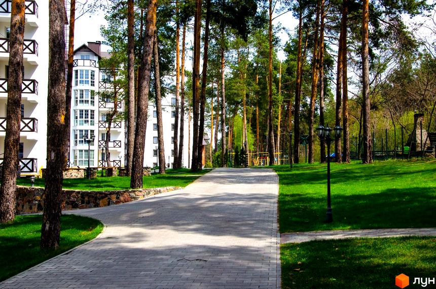Житловий комплекс DESNA residence: білі фасади та сосни. Територія з доріжками, газонами та ліхтарями.