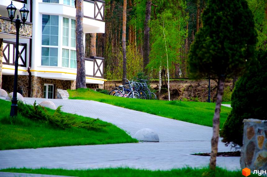 ЖК DESNA residence – біла будівля з кам'яною основою та дерев'яними елементами на балконах. Поруч доглянута прибудинкова територія з доріжками та зеленню.