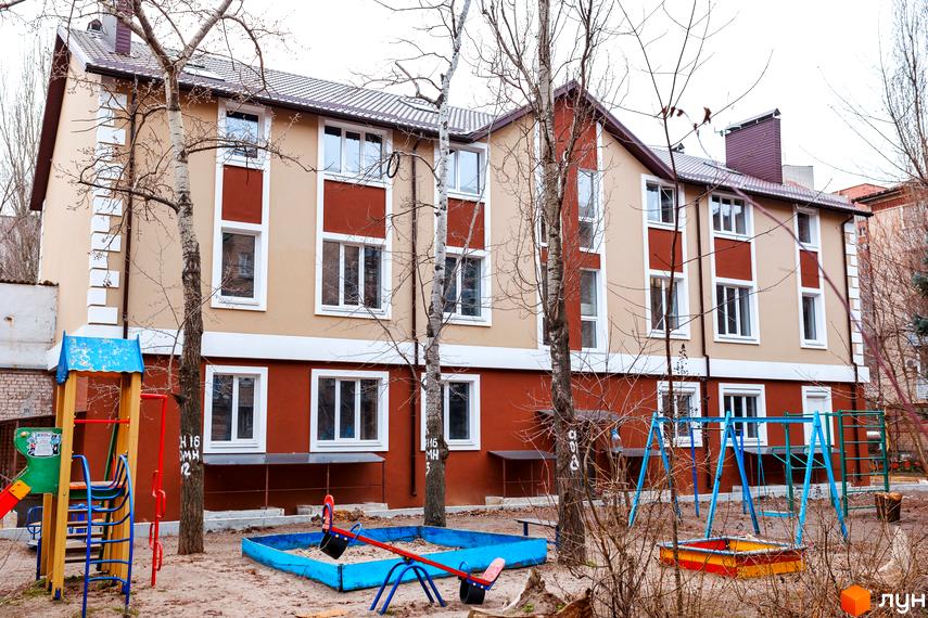 Житловий комплекс Дім на Набережній: двоповерхова будівля з коричневою та бежевою обробкою, вікнами та дитячим майданчиком з гойдалками та пісочницею.