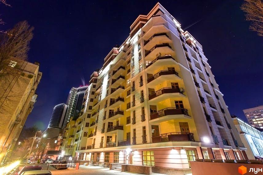 Житловий комплекс ARCH House у Києві. Багатоповерховий будинок з балконами та вікнами, освітлений вночі. Навколо будинку розташовані дерева та припарковані автомобілі.