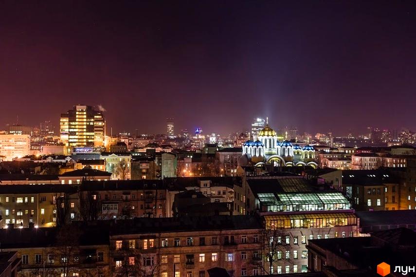 Нічний вид на житловий комплекс ARCH House з освітленими вікнами та будівлями навколо. Комплекс розташований у місті, оточений іншими будинками та міськими вогнями.