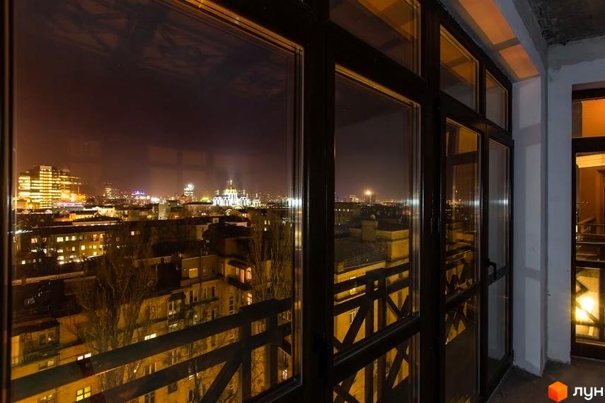 Вид з вікна на нічне місто з освітленими будівлями та балконом ARCH House. Сучасний житловий комплекс з панорамними вікнами та видом на міський пейзаж.