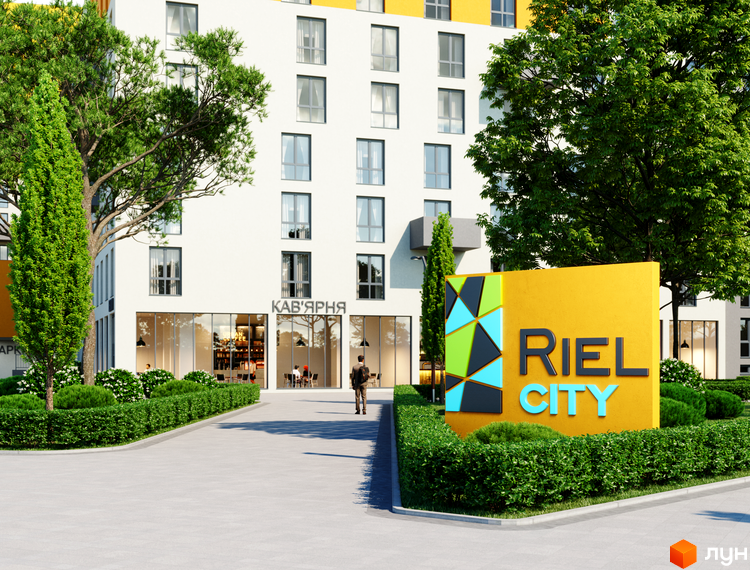 Житловий комплекс Riel City з фасадом біло-жовтого кольору та зеленими деревами на прибудинковій території. Біля входу розташована вивіска з назвою комплексу.