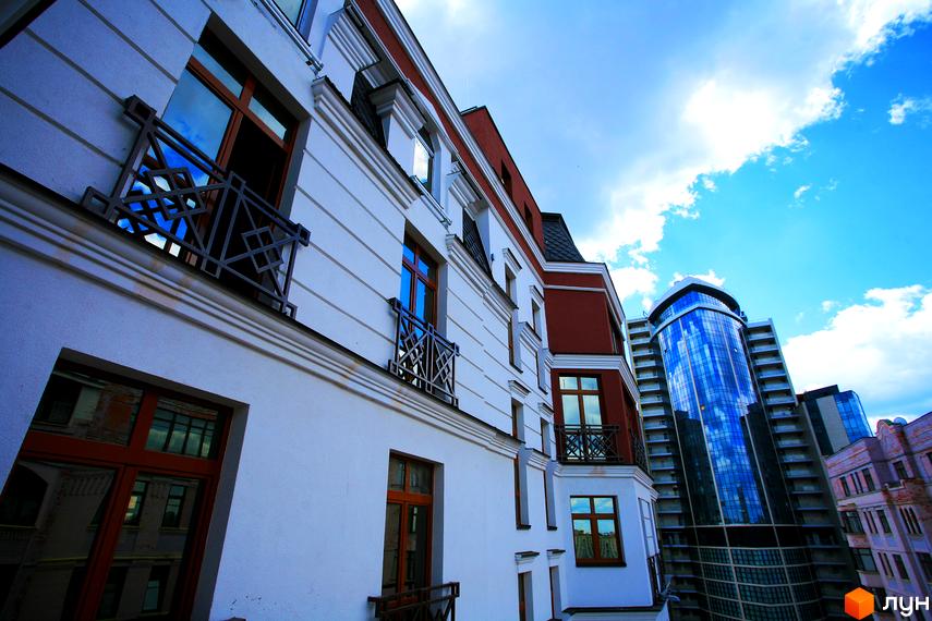 Фасад житлового комплексу ARCH House з білими та червоними елементами, вікнами з коричневими рамами та кованими балконами. На задньому плані видно сучасну скляну новобудову.