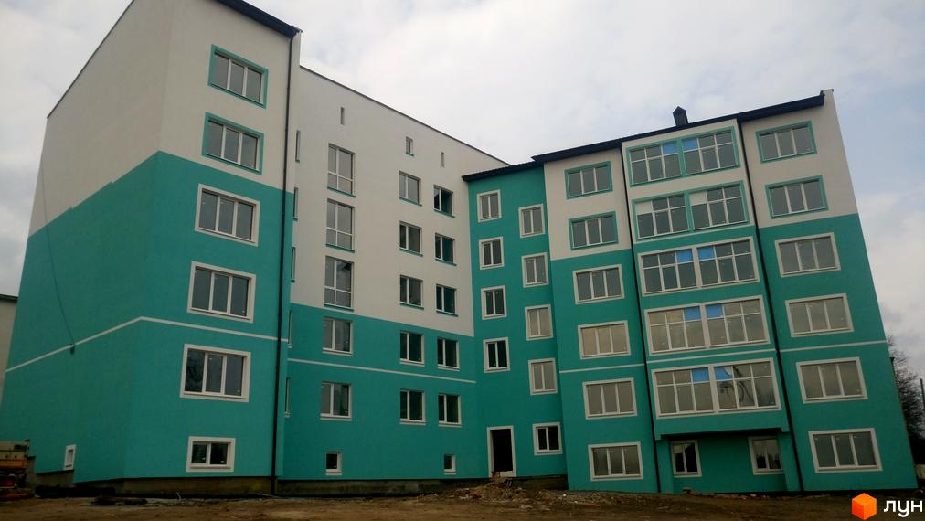 Зовнішній вигляд Новобудови Молодіжний XXI: багатоповерховий будинок з біло-блакитним фасадом та великими вікнами. Навколо будинку будівельний майданчик.