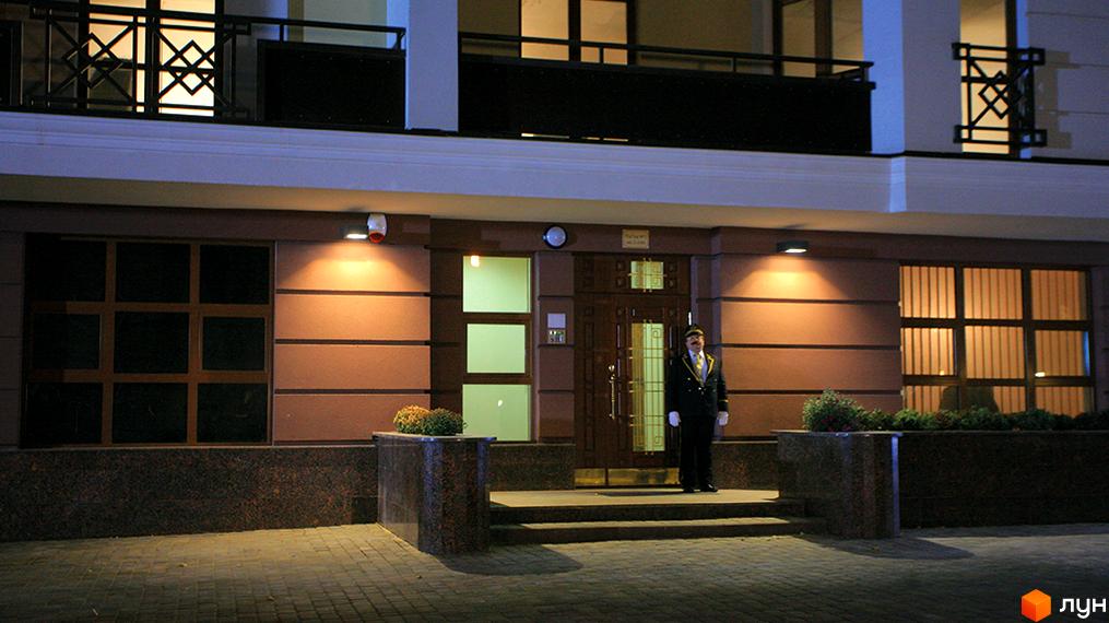 Зовнішній вигляд житлового комплексу ARCH House з охоронцем біля входу. Будинок має коричневий фасад та великі вікна.