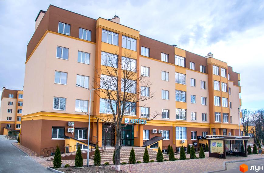 Житловий комплекс Дмитрівський - сучасна новобудова з коричнево-бежевим фасадом та великими вікнами. Перед будинком розташовані зелені насадження та доглянута прибудинкова територія.