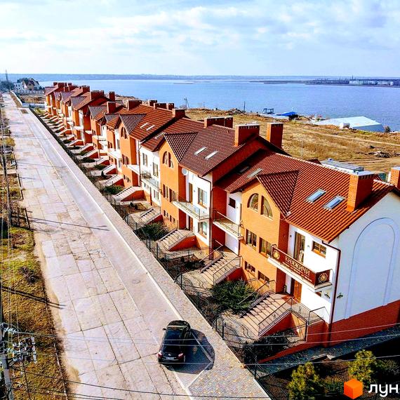 Вид на ряд котеджів КМ Княжичі з теракотовими дахами та біло-цегляними фасадами. Поруч дорога та зелені насадження.