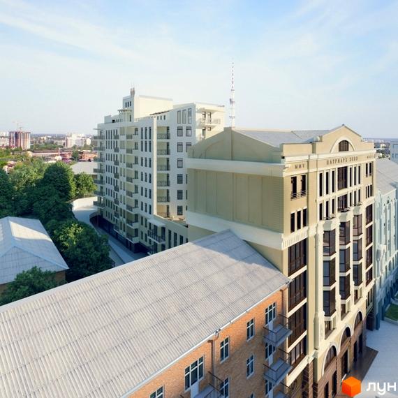 Висотна будівля Клубний будинок „Патріарх Холл“ з балконами та панорамними вікнами. Навколо будинку розташовані інші будівлі та зелені насадження.