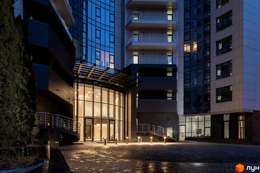 Житловий комплекс Busov Hill з панорамним склінням та вишуканою архітектурою. Територія біля будинку освітлена ліхтарями, що створює затишну атмосферу.