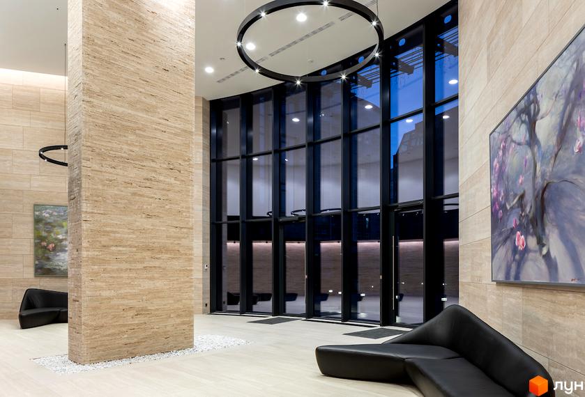 Інтер'єр холу житлового комплексу Busov Hill з дизайнерським диваном та великими вікнами. Сучасний дизайн та оздоблення стін натуральним каменем.
