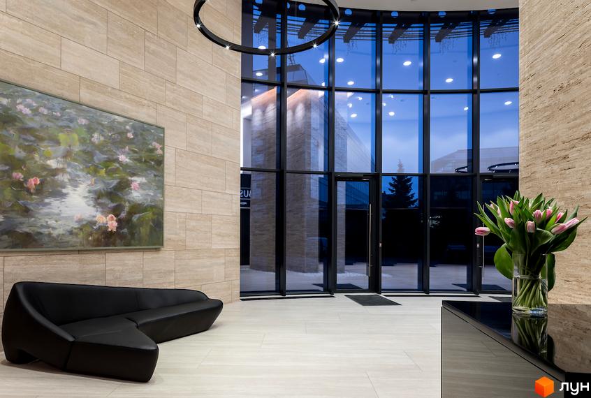 Інтер'єр лобі житлового комплексу Busov Hill з диваном та картиною. Великі вікна з видом на зовнішній простір.