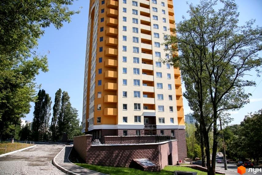 Висотна будівля ЖК Solo Park з жовто-білим фасадом. Поруч розташована прибудинкова територія з деревами та дорогою.