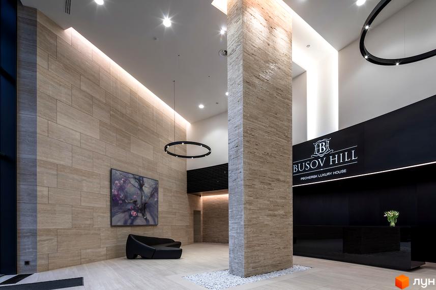 Інтер'єр холу житлового комплексу Busov Hill з великою колоною та картиною на стіні. Сучасний дизайн та оздоблення створюють затишну атмосферу.