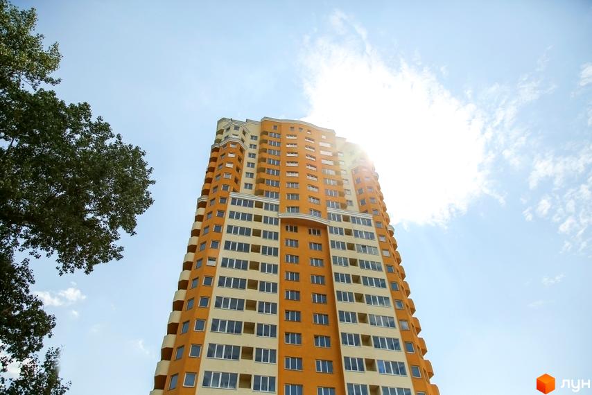Висотна будівля ЖК Solo Park з великою кількістю вікон на тлі блакитного неба. Поруч видніється зелень дерев.