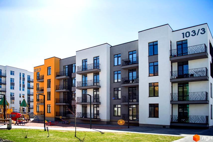 Новобудова Європейка з яскравим жовтим фасадом та сірими вставками. Поруч дитячий майданчик з гірками та гойдалками.