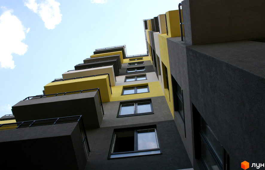 ЖК Енергія плюс: багатоповерховий будинок з виступаючими балконами сірого та жовтого кольорів. Фасад новобудови має геометричні форми.