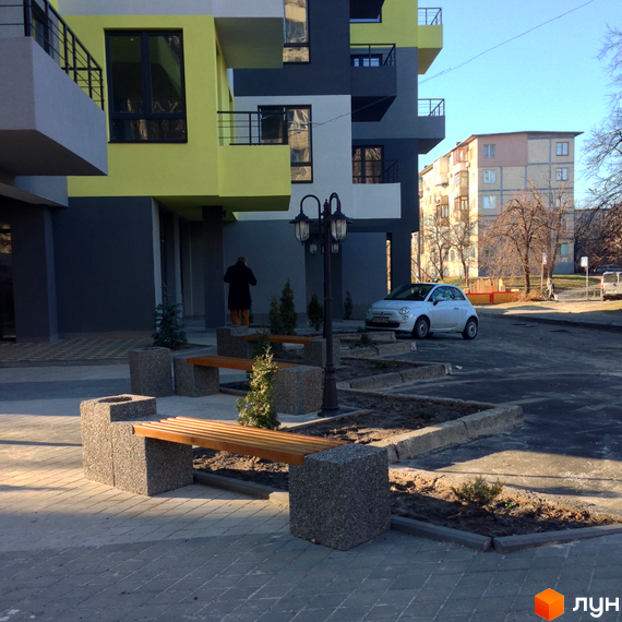 Житловий комплекс Енергія плюс. Будинок з яскравою жовтою та сірою обробкою, прибудинкова територія з лавками та ліхтарем.