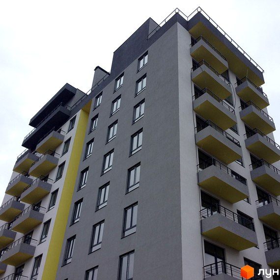 Зовнішній вигляд новобудови ЖК Енергія плюс з сірими та жовтими фасадами, балконами та великою кількістю вікон. Вид знизу на багатоповерховий будинок.