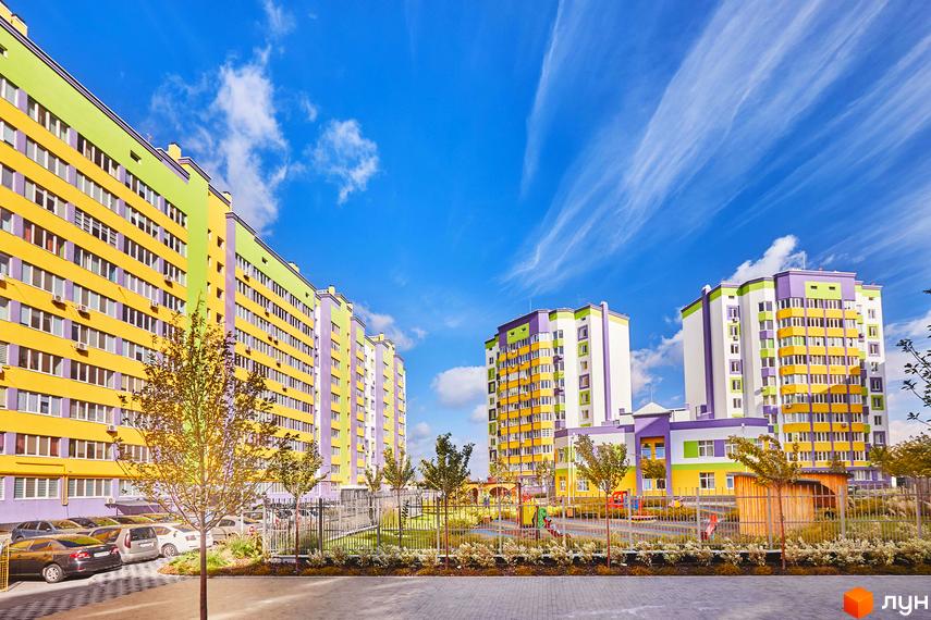 Житловий комплекс Щасливий на Яблуневій. Багатоповерхові будинки яскравих кольорів: жовтого, салатового та фіолетового. На прибудинковій території дитячий майданчик та парковка.